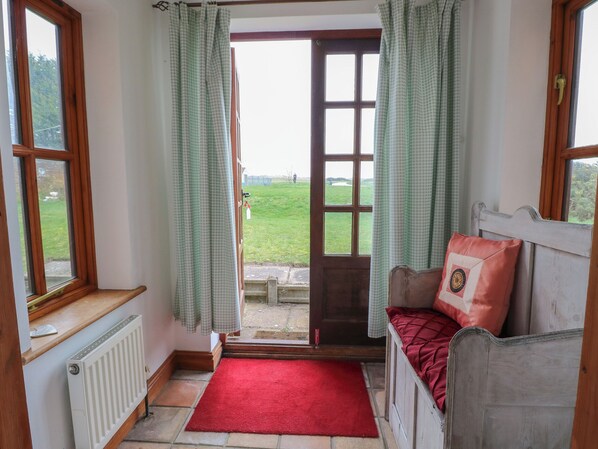 A room with a wooden bed, a red rug, a view of a green field through a door, and a window with a curtain. - Mabby (Great Yarmouth)