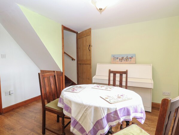 Un coin repas avec une table dressée pour deux personnes, un piano et un escalier menant à une autre pièce.