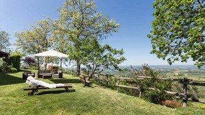 Eine grüne Außenanlage mit einer Bank, einer überdachten Sitzgelegenheit und Blick auf die Landschaft.