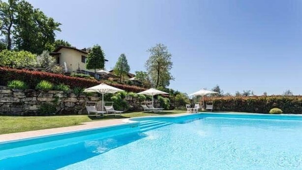 Ein Pool mit Liegestühlen und Sonnenschirmen, umgeben von einer Steinmauer und Grünpflanzen.