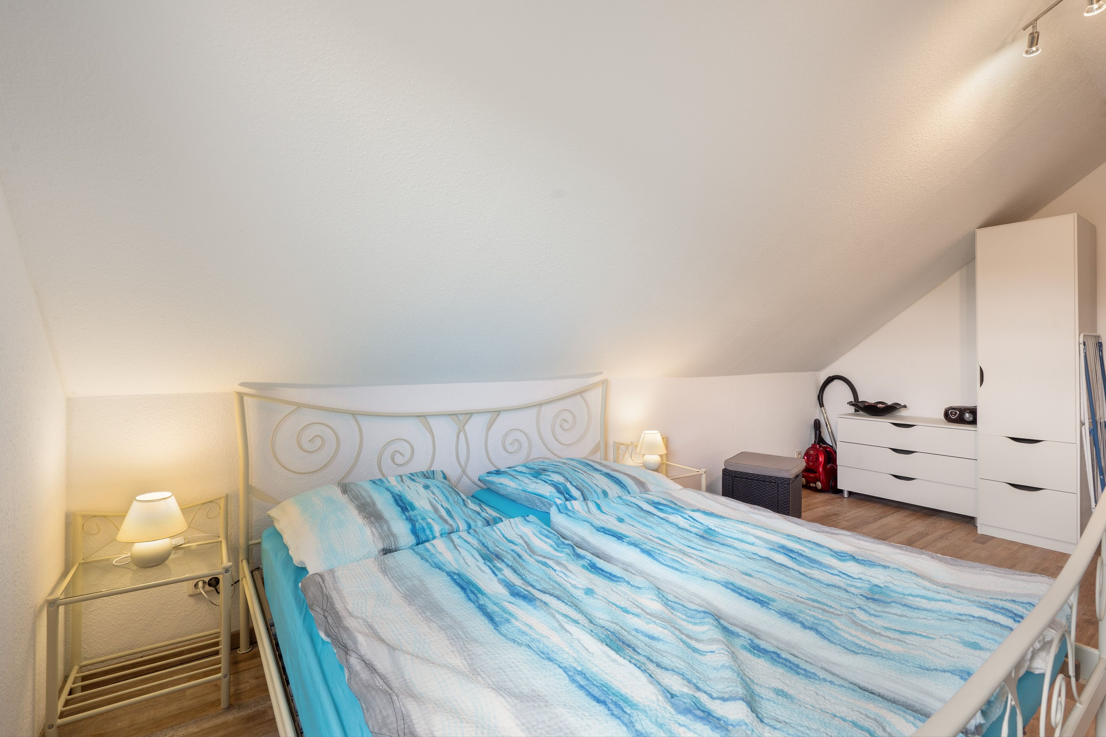 Ein Schlafzimmer mit einem Bett, einem Nachttisch, einer Lampe, einer Kommode und einem Staubsauger.