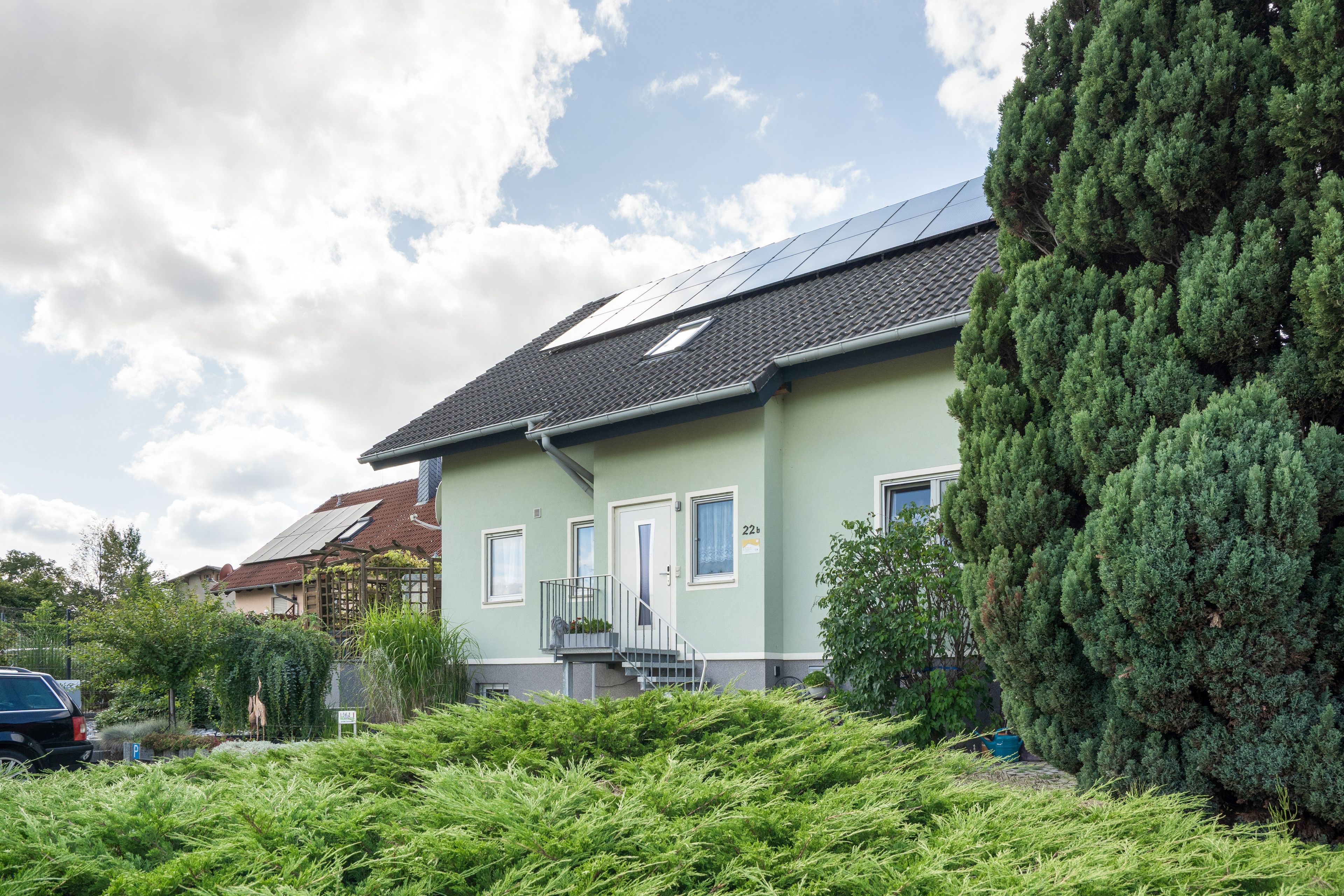 Ein Wohngebäude mit Satteldach, Solaranlage und einem gepflegten Garten.