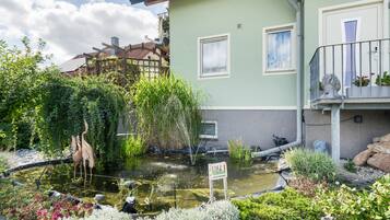 Ein Wohngebäude mit Teich, einer Holz-Pergola und einem Balkon mit Blumentöpfen.
