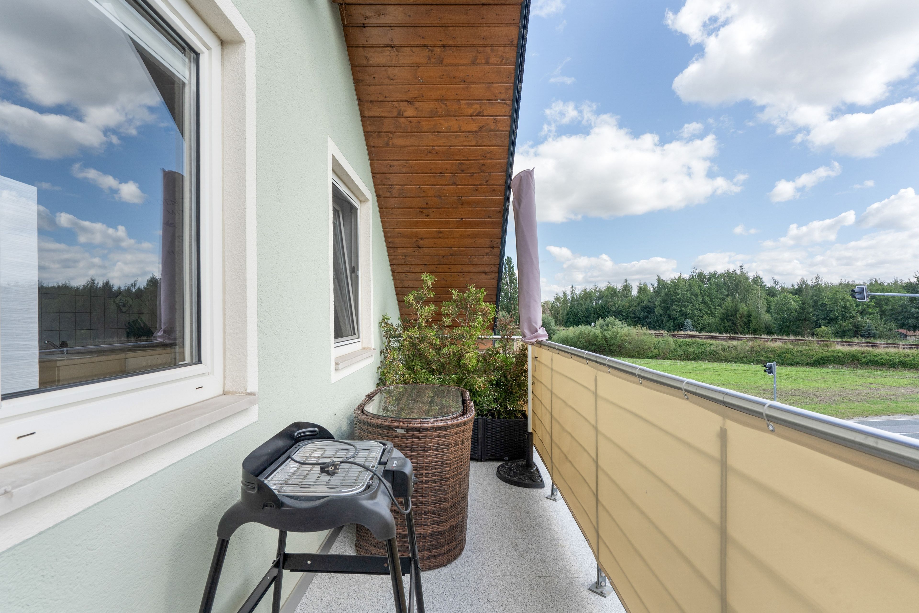 Ein Balkon mit einem Korbstuhl, einem kleinen Tisch und einem Blumentopf.