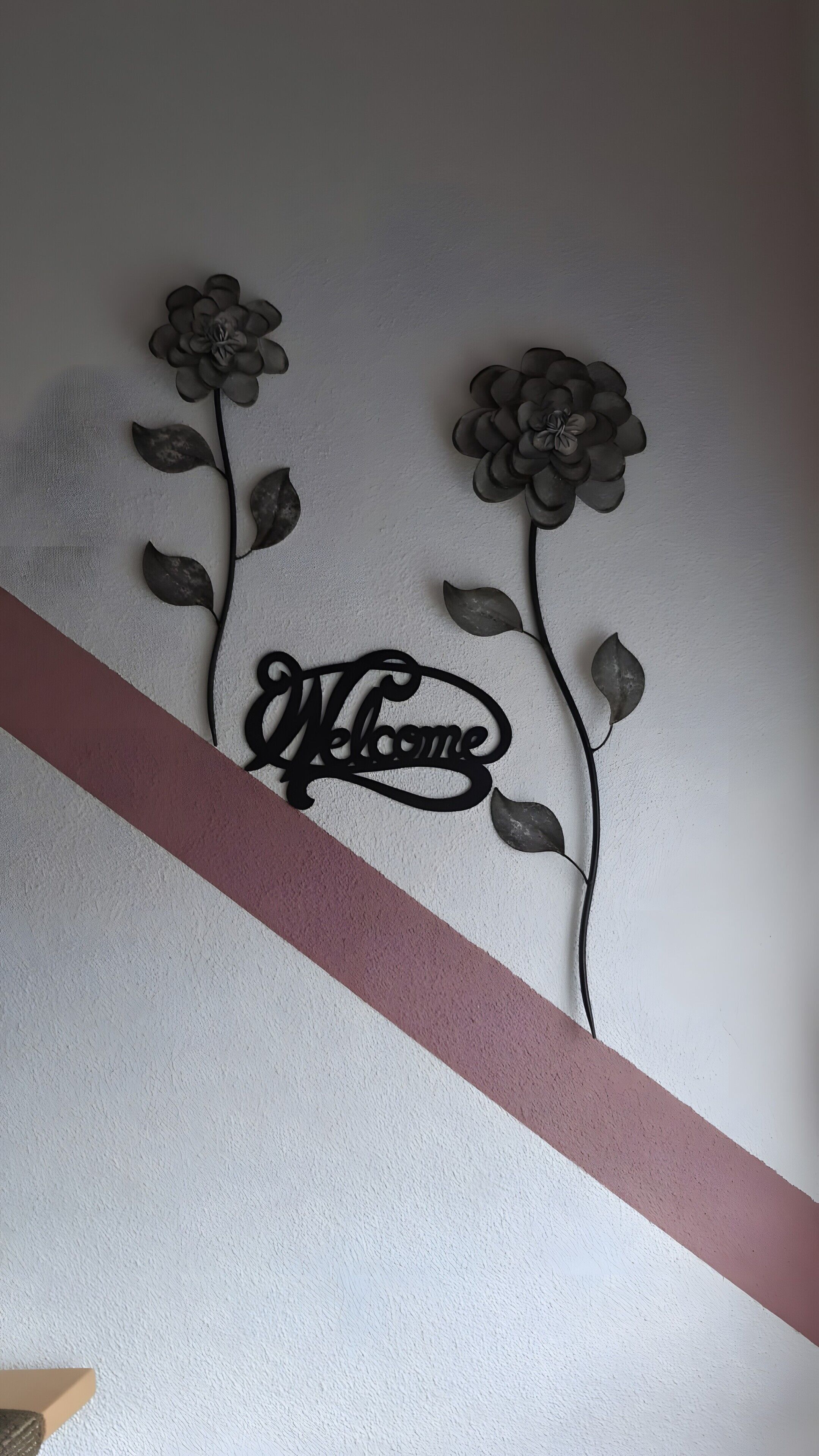 A wall with a decorative metal sign that reads 'Welcome' and two stylized flowers.