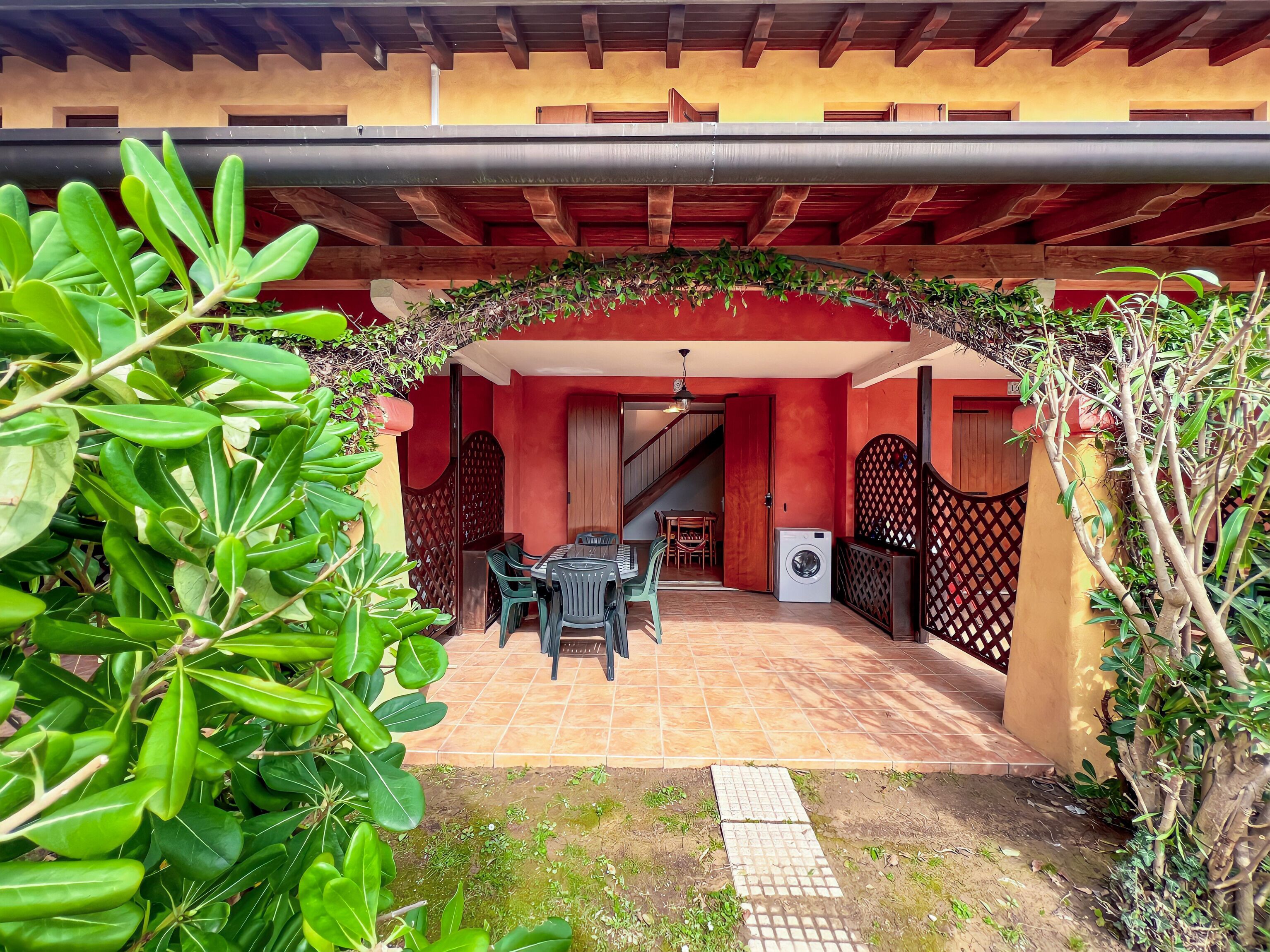 An outdoor patio with a covered seating area, a washing machine, and a staircase leading to an upper level.