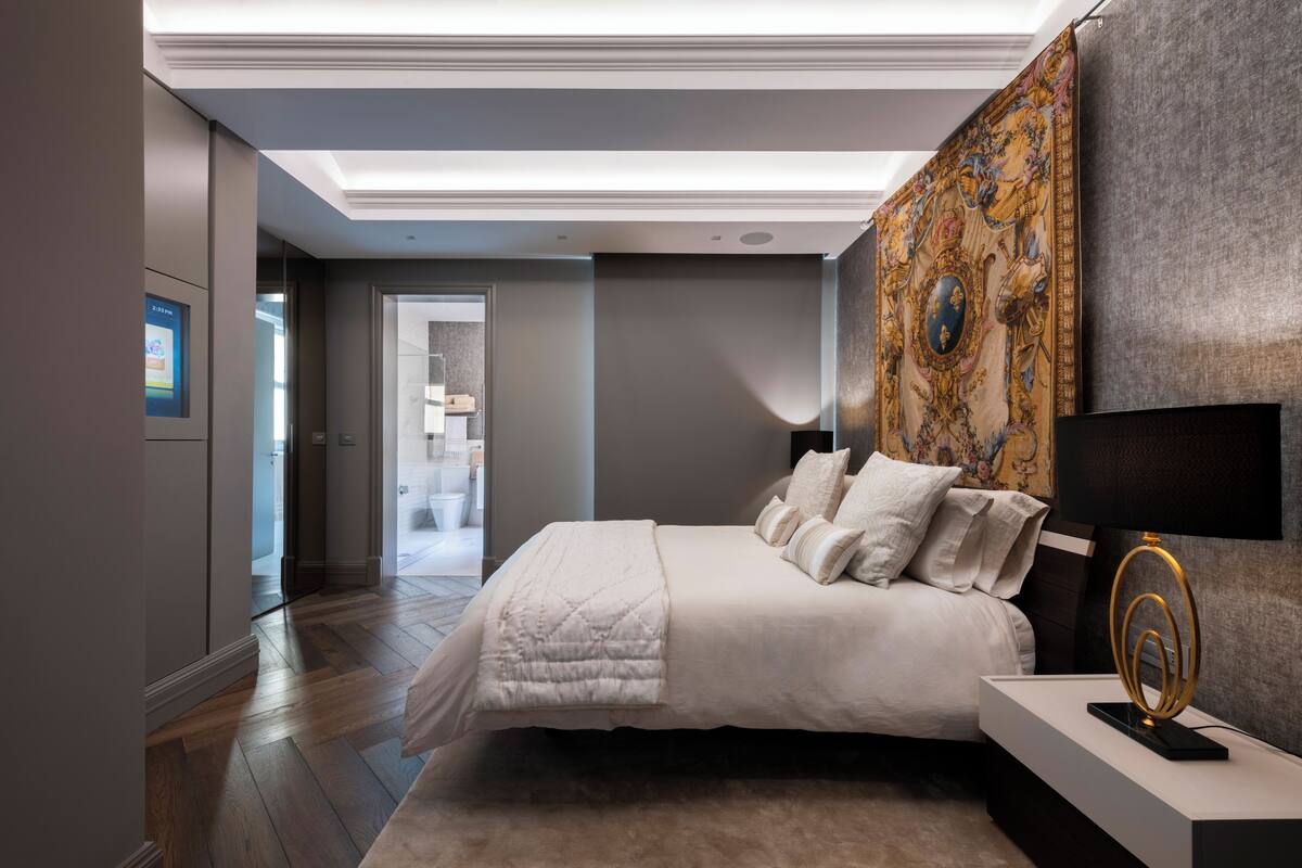 Une chambre à coucher moderne avec un grand lit, une table de chevet avec une lampe, une tapisserie murale et une vue sur la salle de bain.