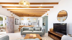 Una sala de estar moderna con sofá, mesa de centro, televisor y cocina al fondo.