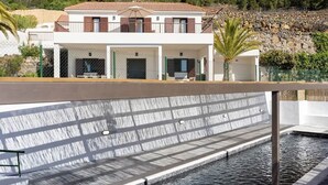 Un edificio moderno con zona de piscina, que incluye una fuente de agua y un muro de piedra.