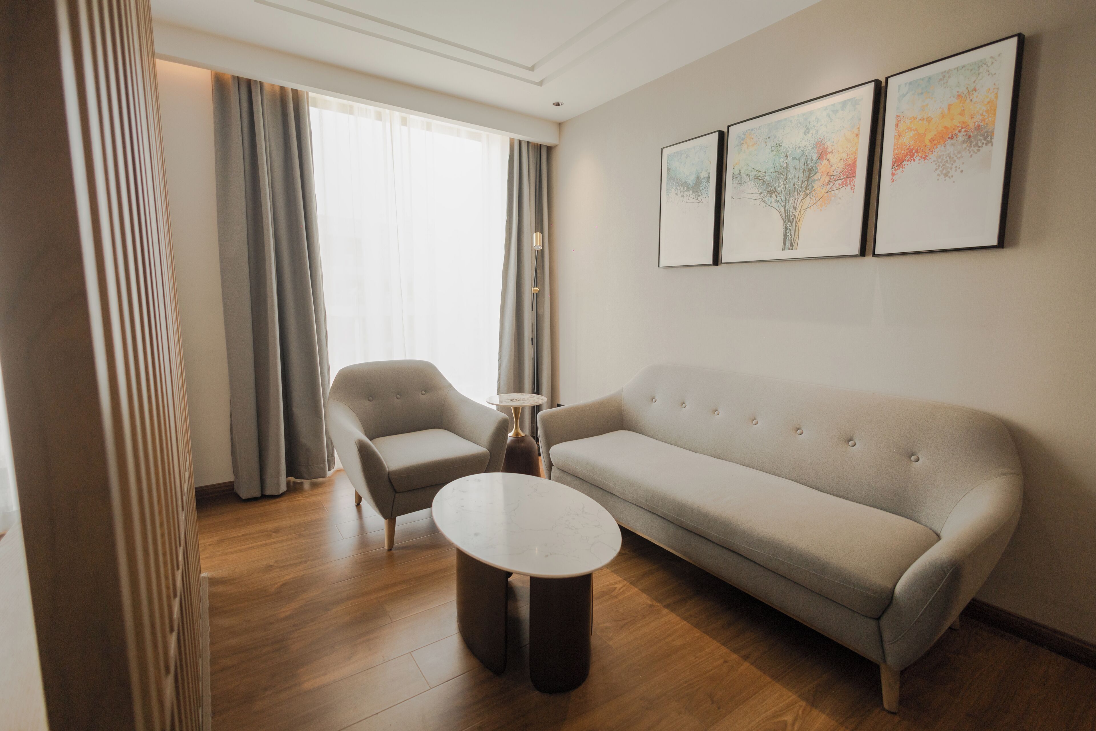 A modern living room with a sofa, two armchairs, a coffee table, and a floor lamp. There are three framed artworks on the wall.
