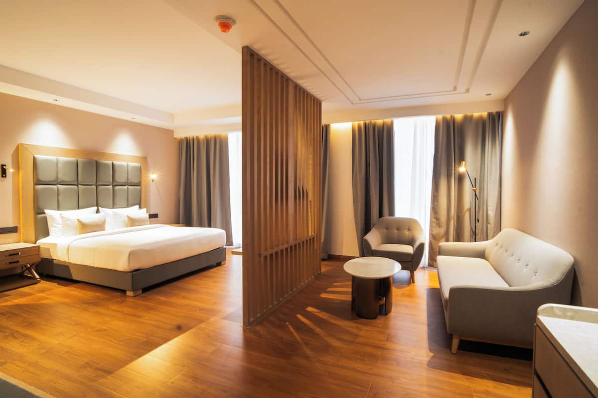 A modern hotel room with a large bed, a sofa, a chair, and a small table.