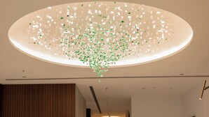 Un hall d’entrée moderne agrémenté d’un grand lustre, d’un comptoir de réception et d’un mur décoratif en bois.