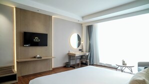 Une chambre d’hôtel moderne avec un grand lit, un bureau avec une chaise, un téléviseur fixé au mur, un miroir rond et une petite table avec une lampe.