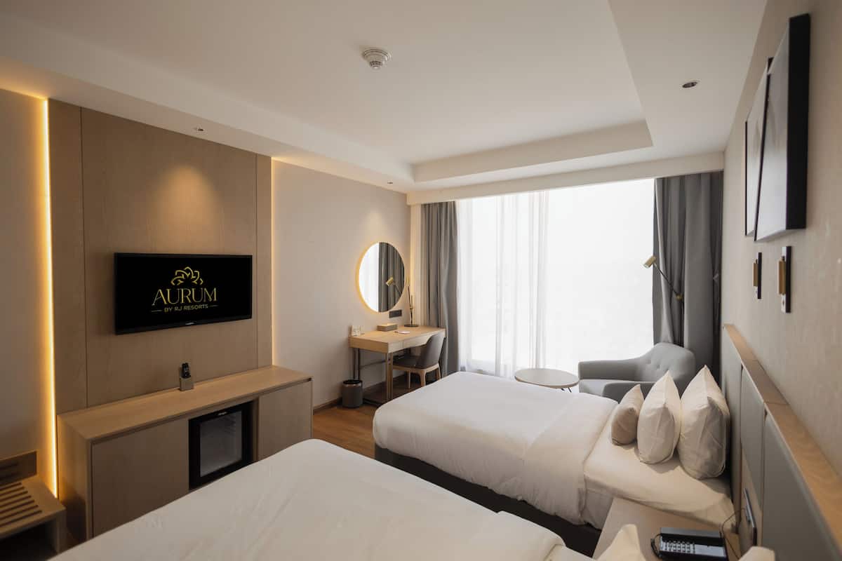 A hotel room with two beds, a desk, a chair, a TV, and a window with curtains.