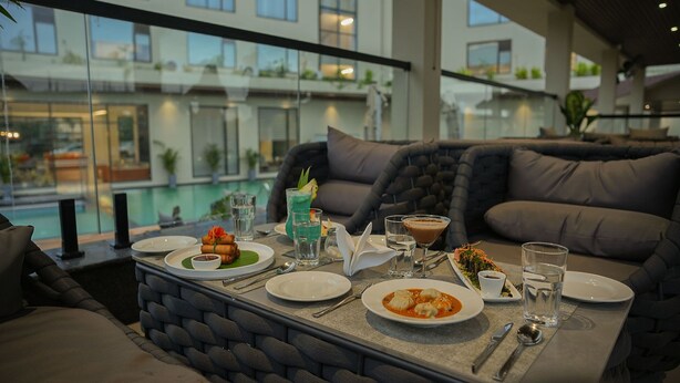 Un coin repas avec vue sur la piscine, une table dressée avec des assiettes, des verres et un cocktail.