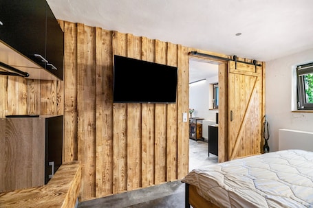 A bedroom with a wooden wall, a TV mounted above a bed, and a sliding door leading to another room.. Apartment 'Fewo Tostner Burgblick 2P Terrasse' with Mountain View, Private Terrace and Wi-Fi
