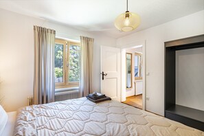 A bedroom with a bed, a radiator, a window with curtains, a door, and a hanging light fixture. - Tostner Burgblick Apartment – Quiet Green Setting with Balcony (Feldkirch)