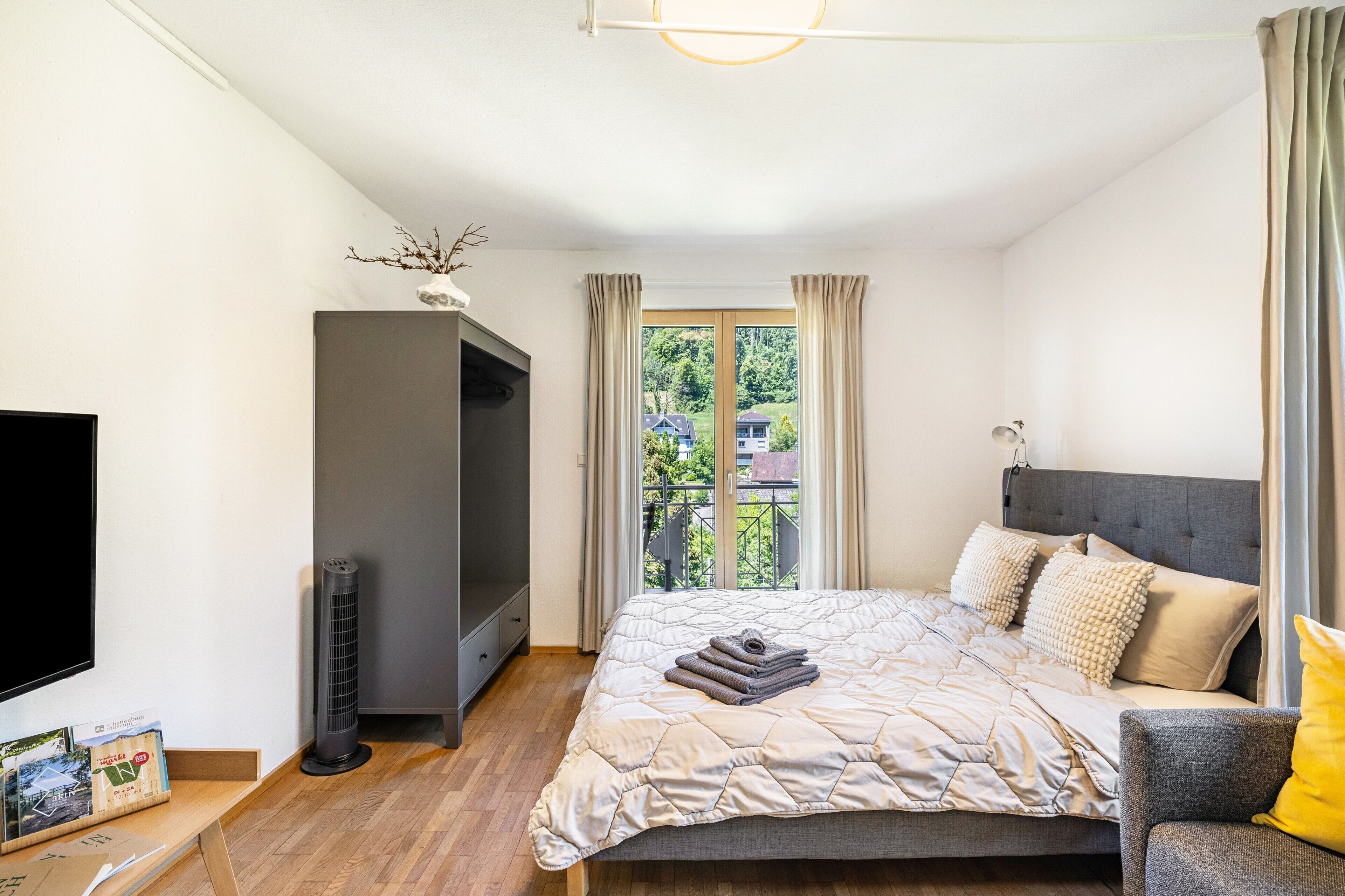 Ein Schlafzimmer mit Bett, Fernseher, Heizung und einem Fenster mit Vorhängen.