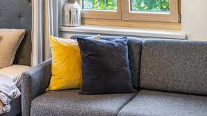 Un canapé gris avec deux coussins, une fenêtre donnant sur un paysage verdoyant et un vase posé sur une étagère.