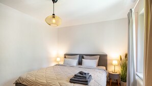Une chambre à coucher avec un lit, des lampes de chevet, une plante en pot et une fenêtre avec des rideaux.