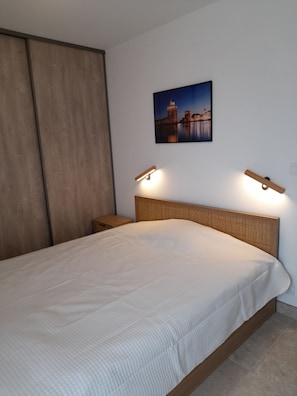 Une chambre à coucher avec un lit, une tête de lit en bois, des lampes de chevet, une table de chevet et un tableau accroché au mur.