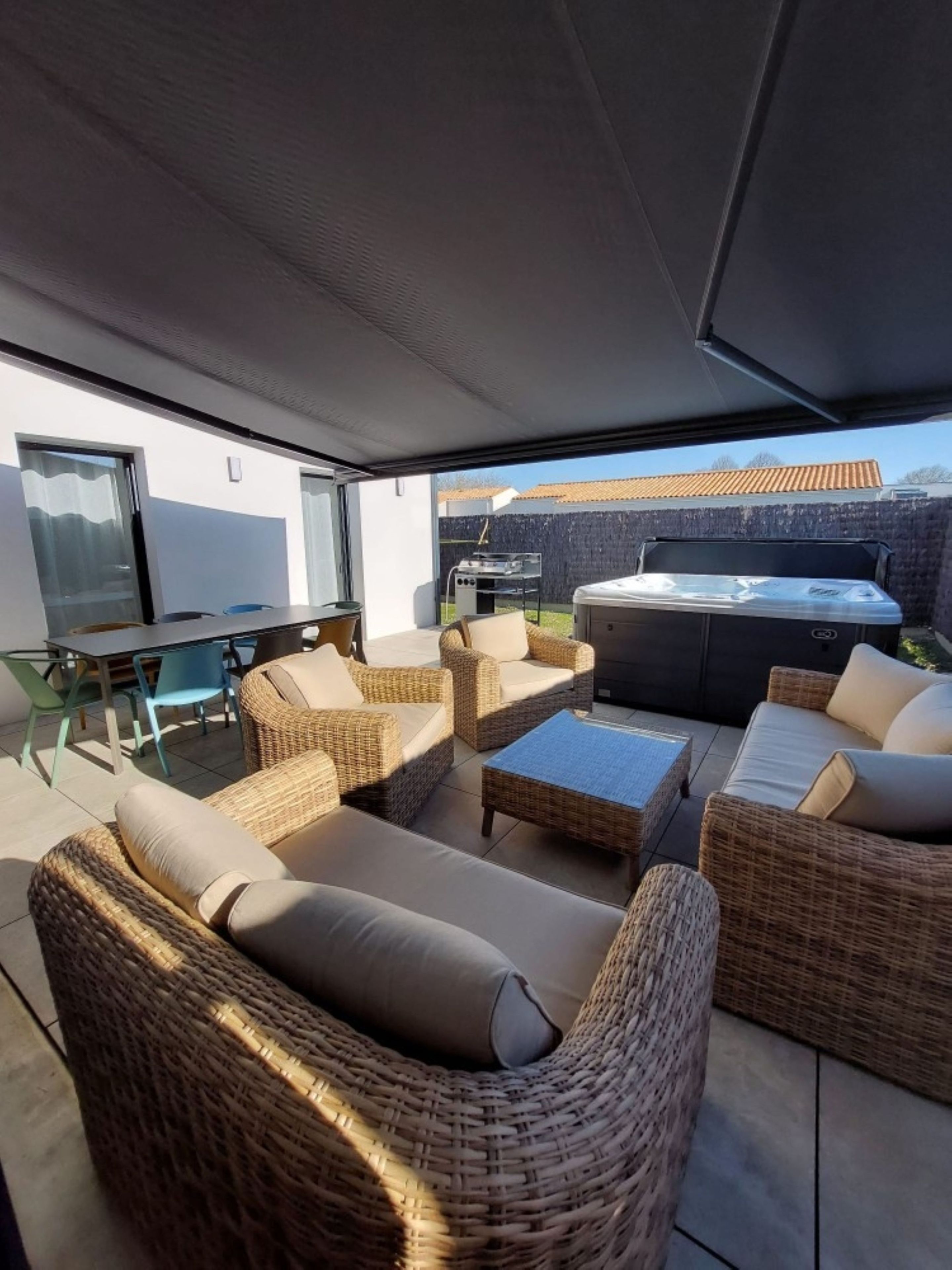 A covered outdoor seating area with wicker furniture and a hot tub.
