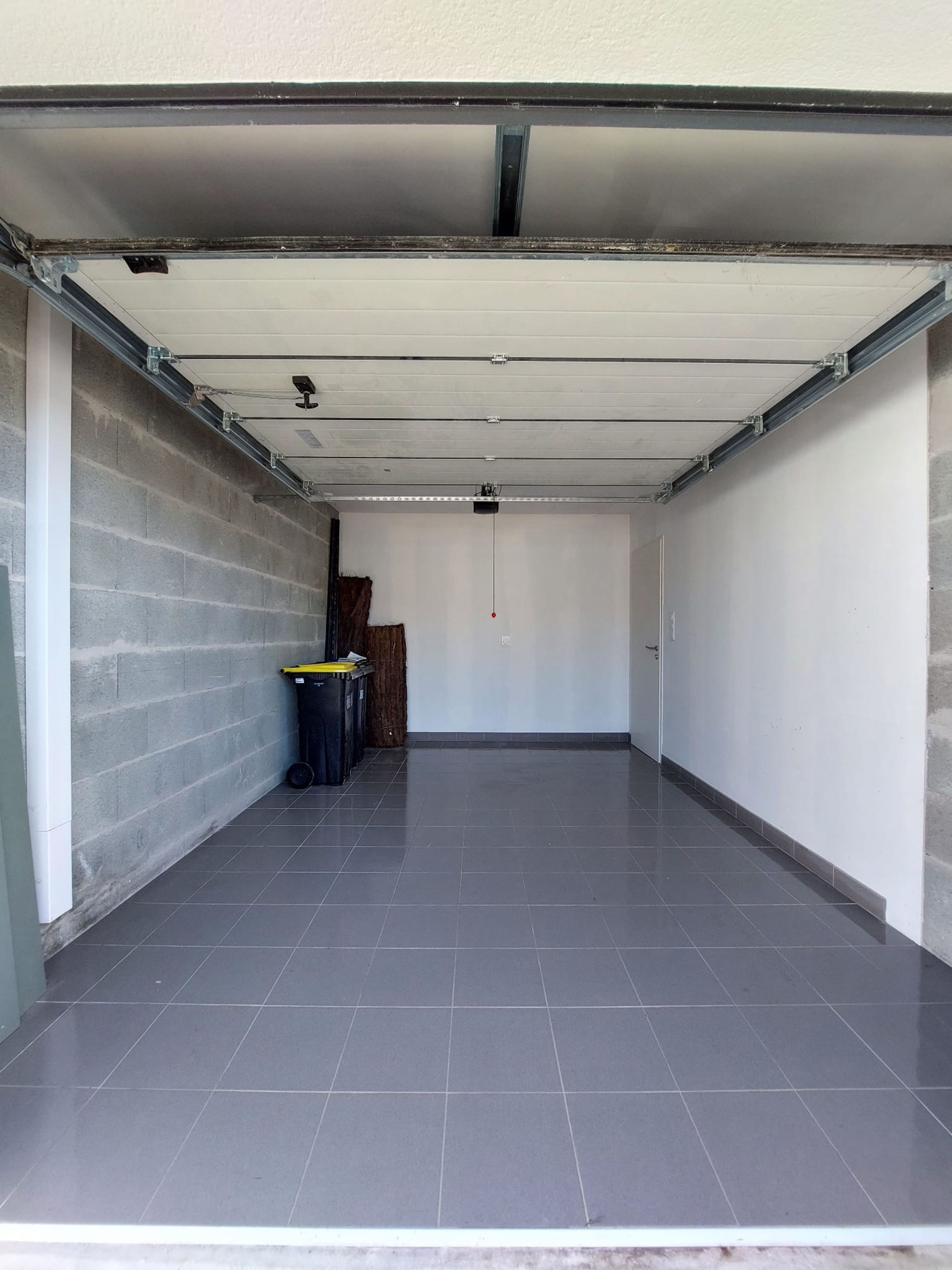 A clean, empty garage with a tiled floor, a white ceiling, and a brick wall.