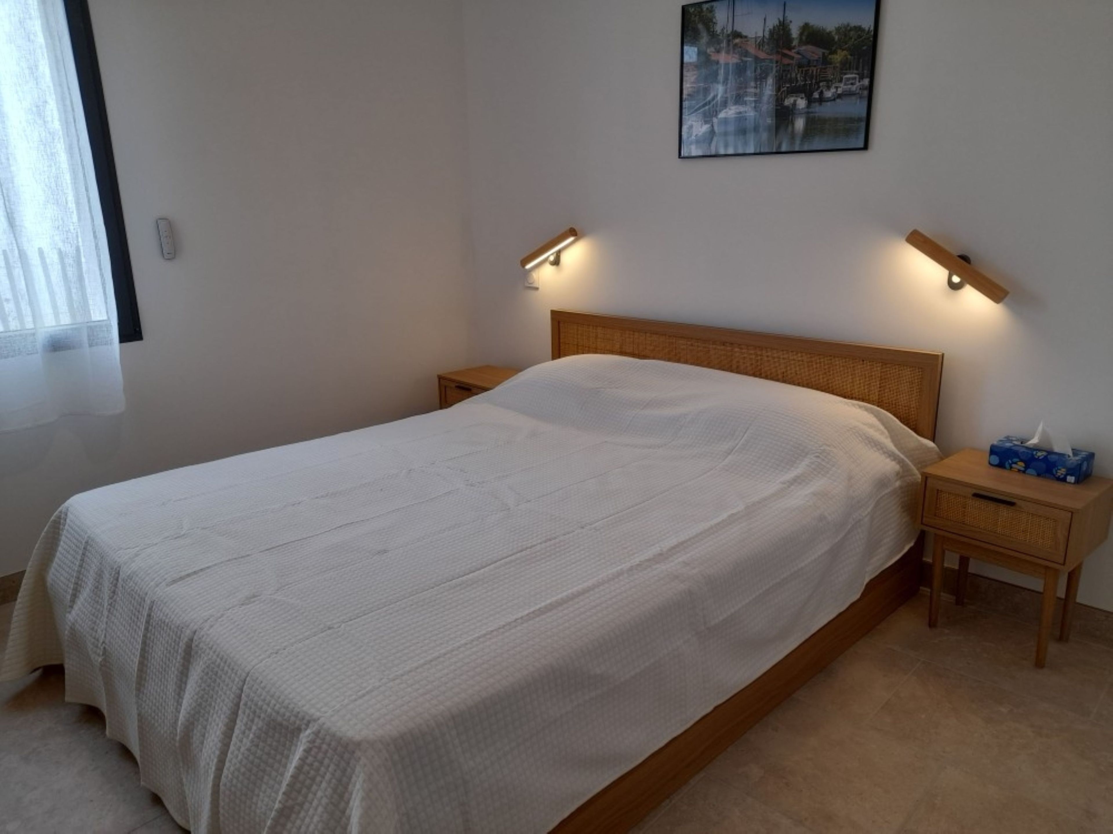 A neatly made bed with a white bedspread, two bedside tables with lamps, and a wall-mounted picture.
