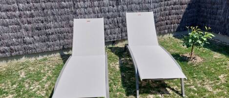Deux fauteuils de relaxation dotés de pieds en métal et d’une assise plane, placés sur une pelouse, avec un mur à texture en arrière-plan.