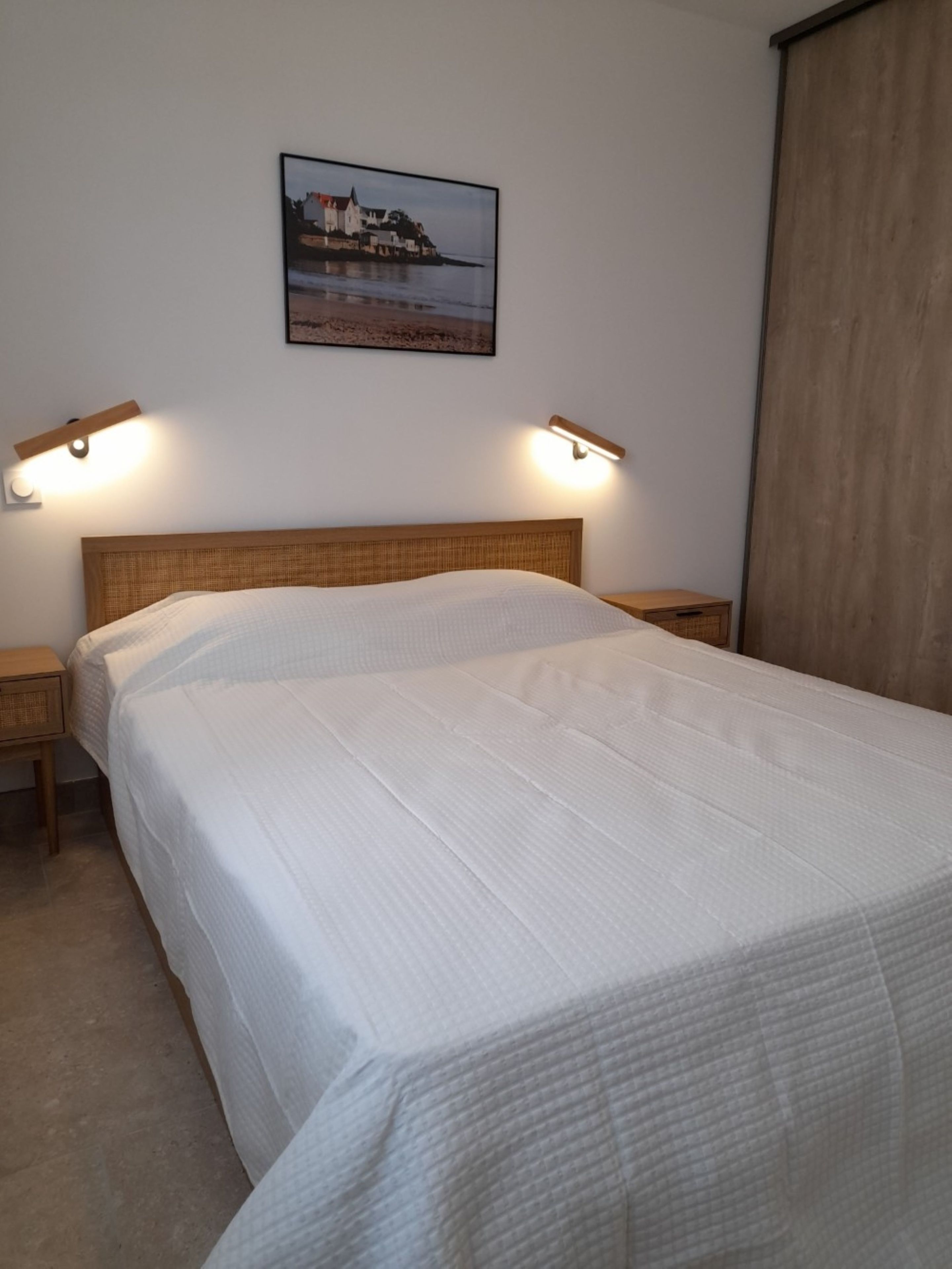 A bedroom with a bed, two bedside tables, a headboard, and a wall-mounted picture.
