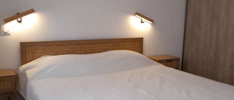 A bedroom with a bed, two bedside tables, a headboard, and a wall-mounted picture.