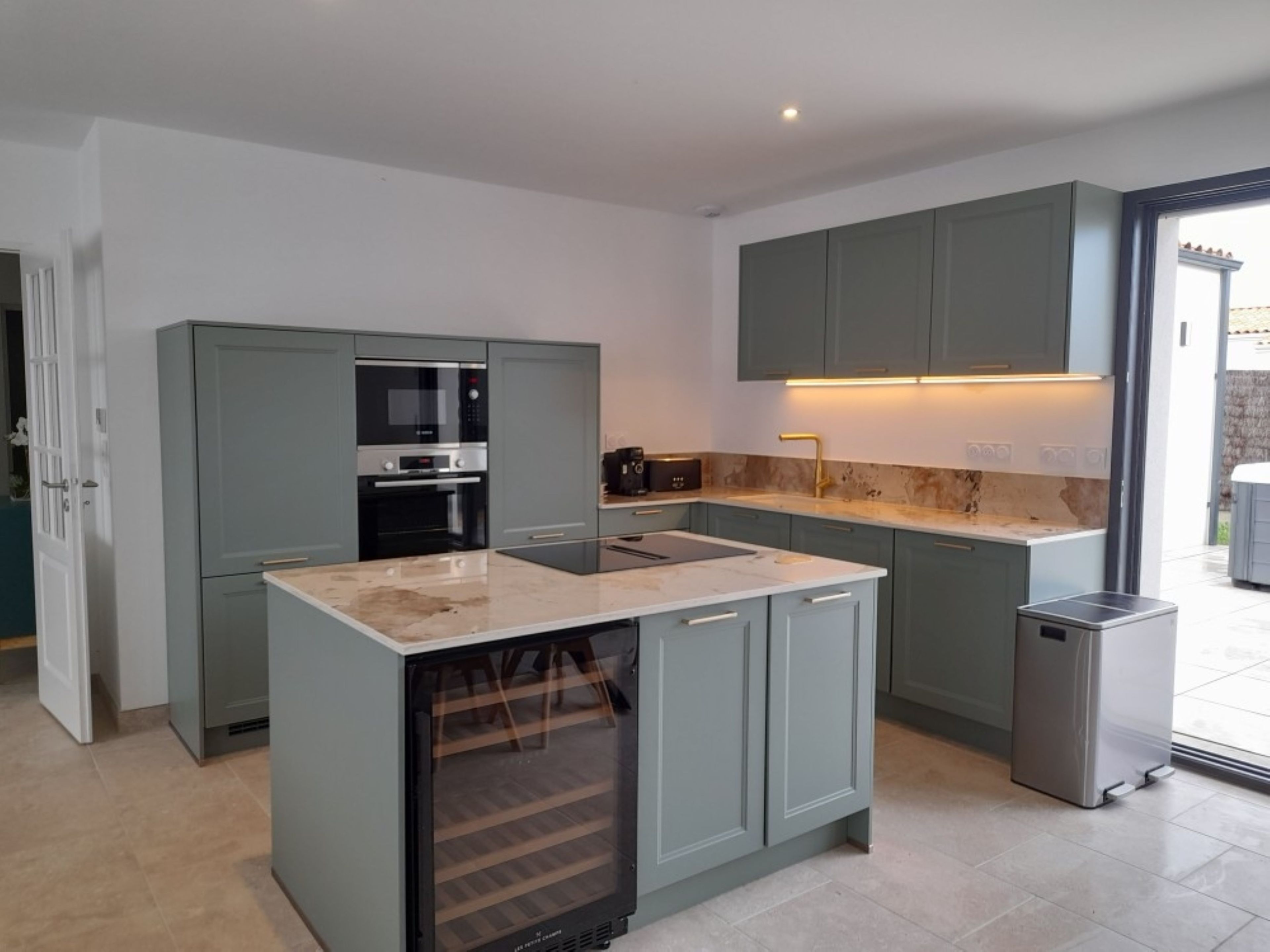 A modern kitchen with grey cabinets, a built-in oven, a microwave, and a stainless steel sink.
