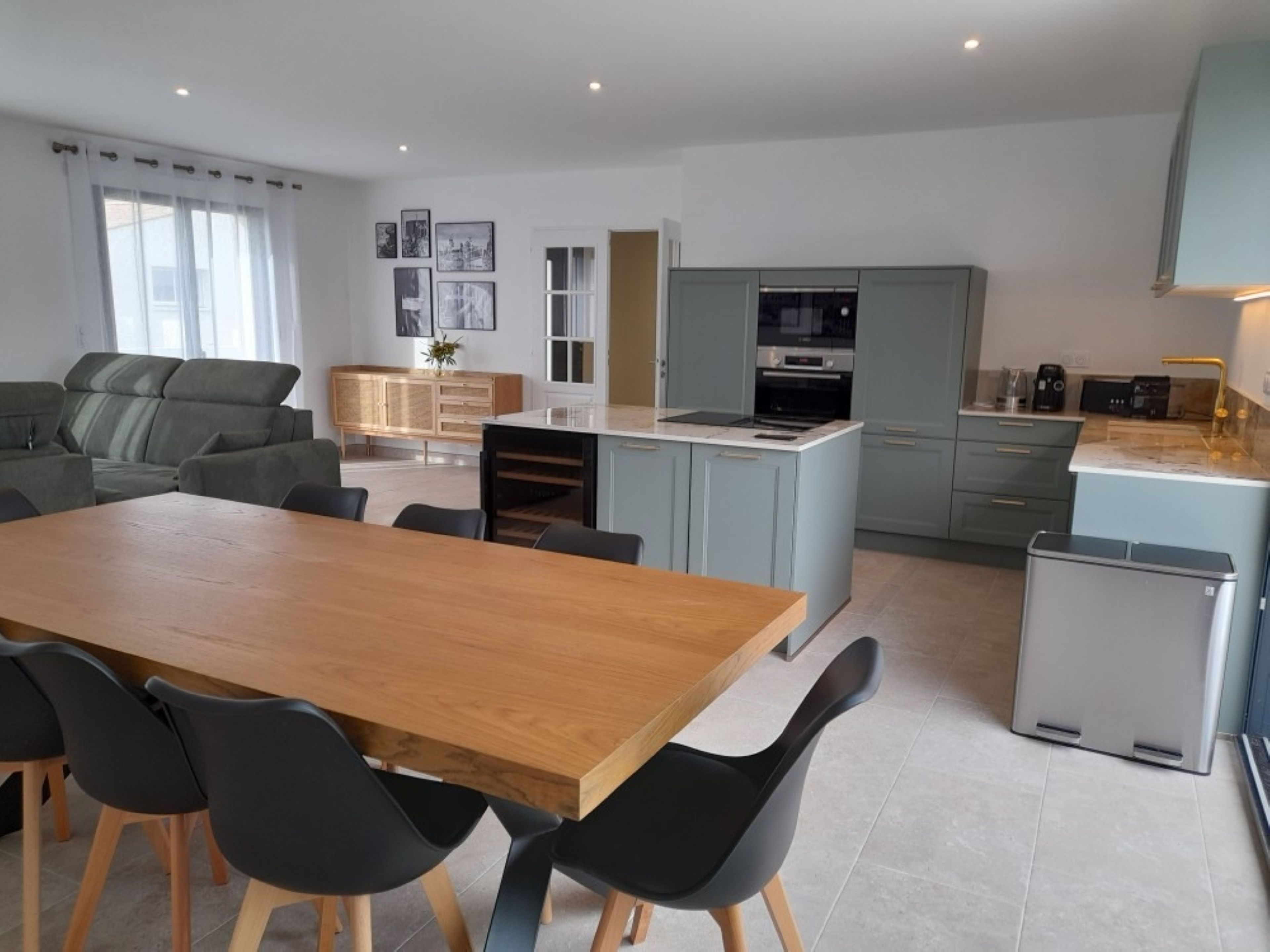 Une cuisine moderne avec un coin repas, des meubles gris et un petit réfrigérateur.