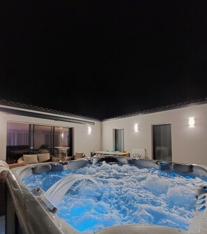 Un bain à remous avec jets d’eau, un coin repas avec une table et des chaises, et une grande fenêtre.