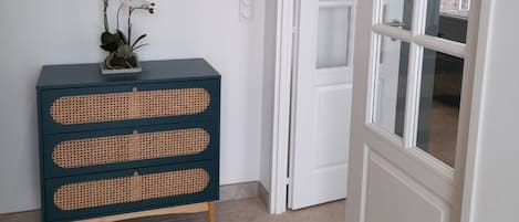 Un pasillo con un mueble azul oscuro con tres cajones, una planta en maceta y un cuadro en la pared.