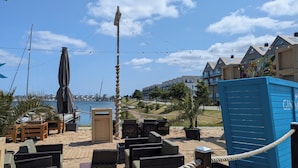 Ett sittområde vid stranden med träsolstolar och ett avspärrningsrep, med utsikt över en småbåtshamn och bostadshus.
