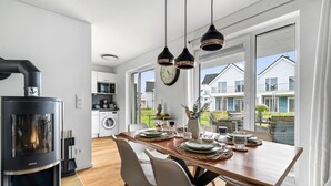 Ett modernt kök med en vedspis från Justus, en matplats med ett träbord för fyra personer och stora fönster med utsikt över de närliggande husen.