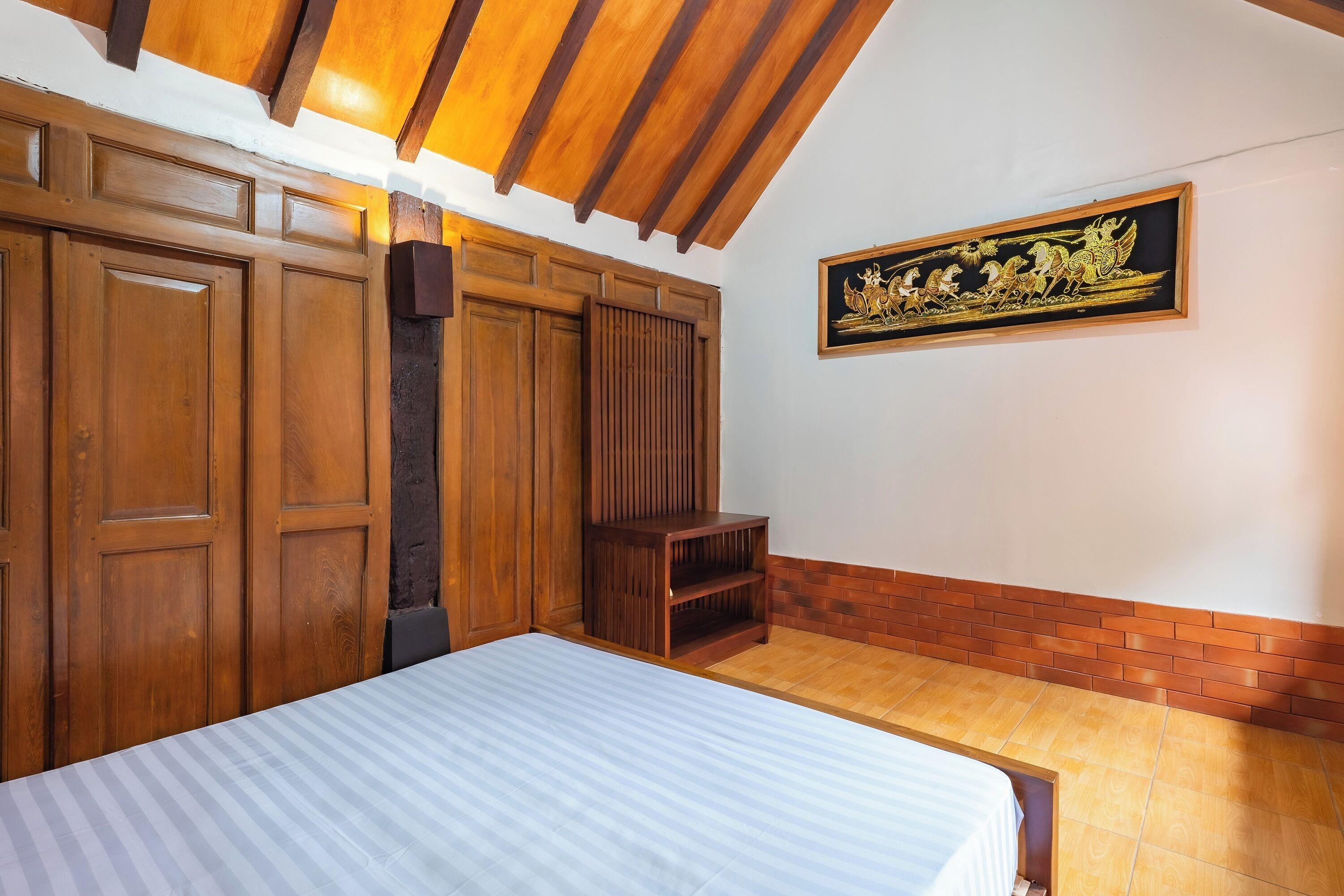 A room with a bed, wooden wardrobe, and a wall-mounted artwork.