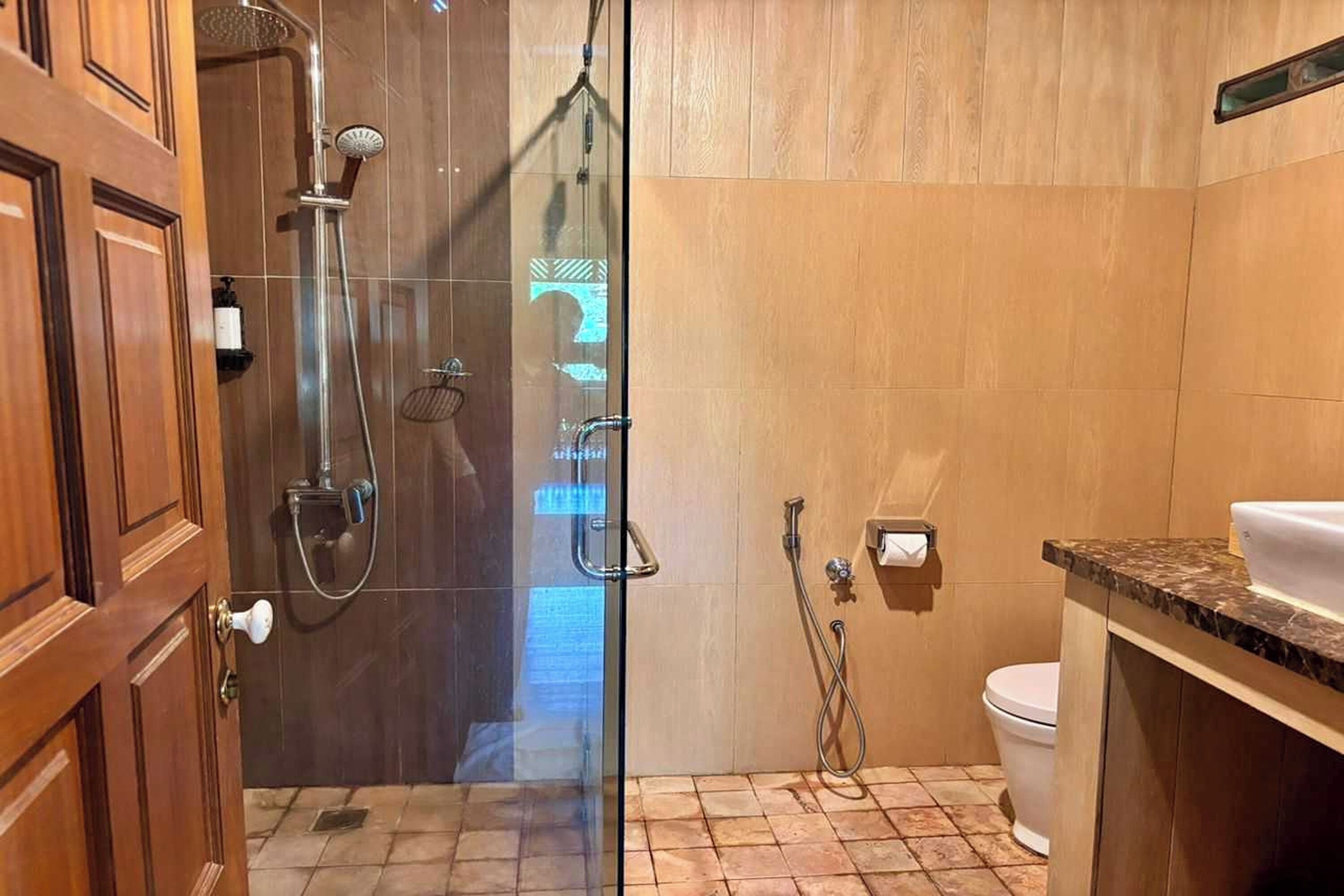 A bathroom with a glass shower enclosure, a toilet, and a sink with a marble countertop.