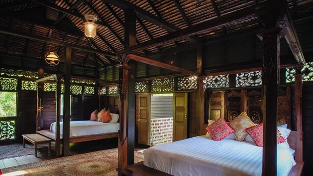 A traditional wooden room with a four-poster bed, a bench, and a table with a bowl.