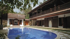 A pool surrounded by a stone patio, a wooden building with a balcony, and a stone wall.