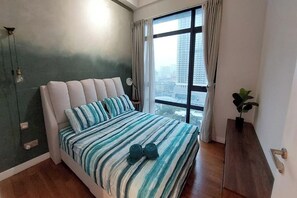 A bedroom with a bed, a window with curtains, a plant, and a view of buildings. - Golden Suites At Majestic Residence Klcc (Kuala Lumpur)