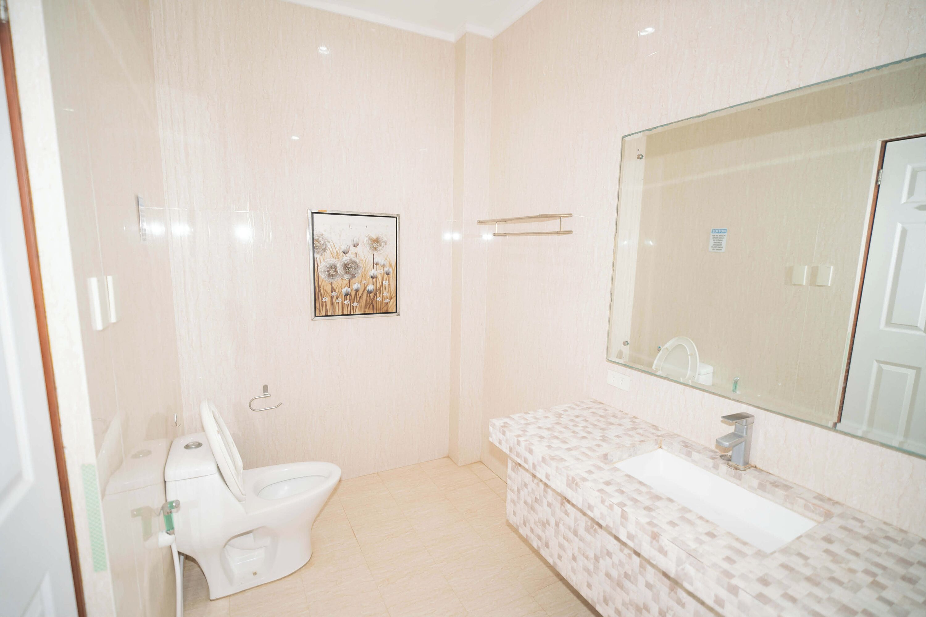 Un baño con inodoro, lavamanos, espejo y un cuadro en la pared.