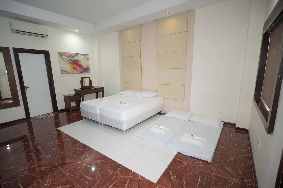 A hotel room with two beds, a bedside table, a mirror, and a painting on the wall.