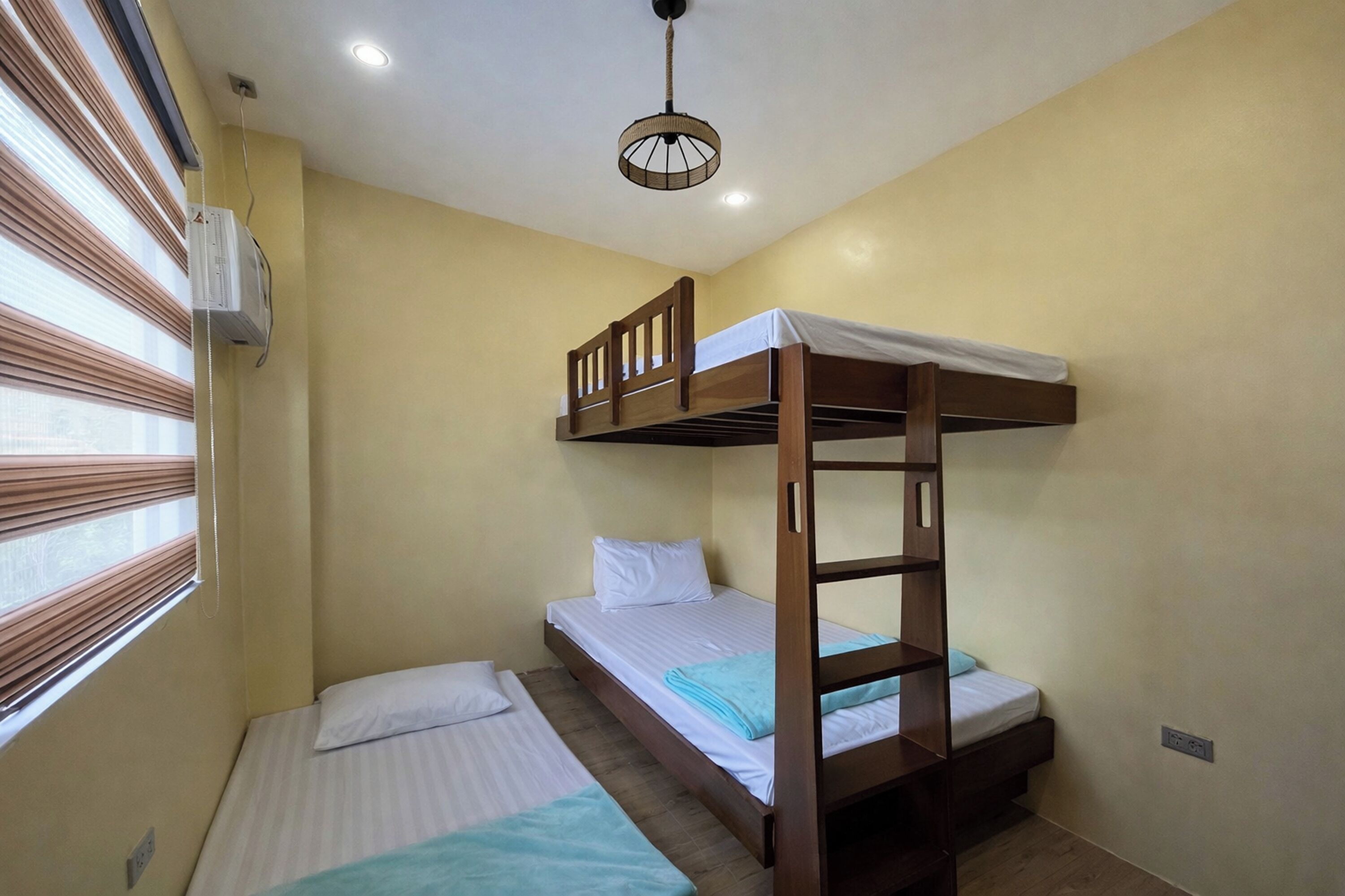 Quarto com duas beliches, janela com persianas, ar condicionado e luminária no teto.
