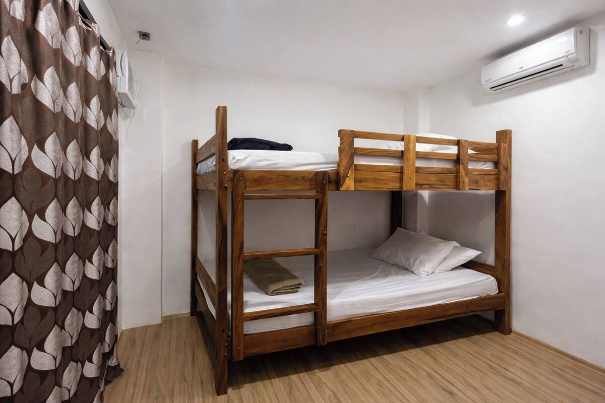 Una cama litera con estructura de madera, colchón blanco y cortina marrón estampada.