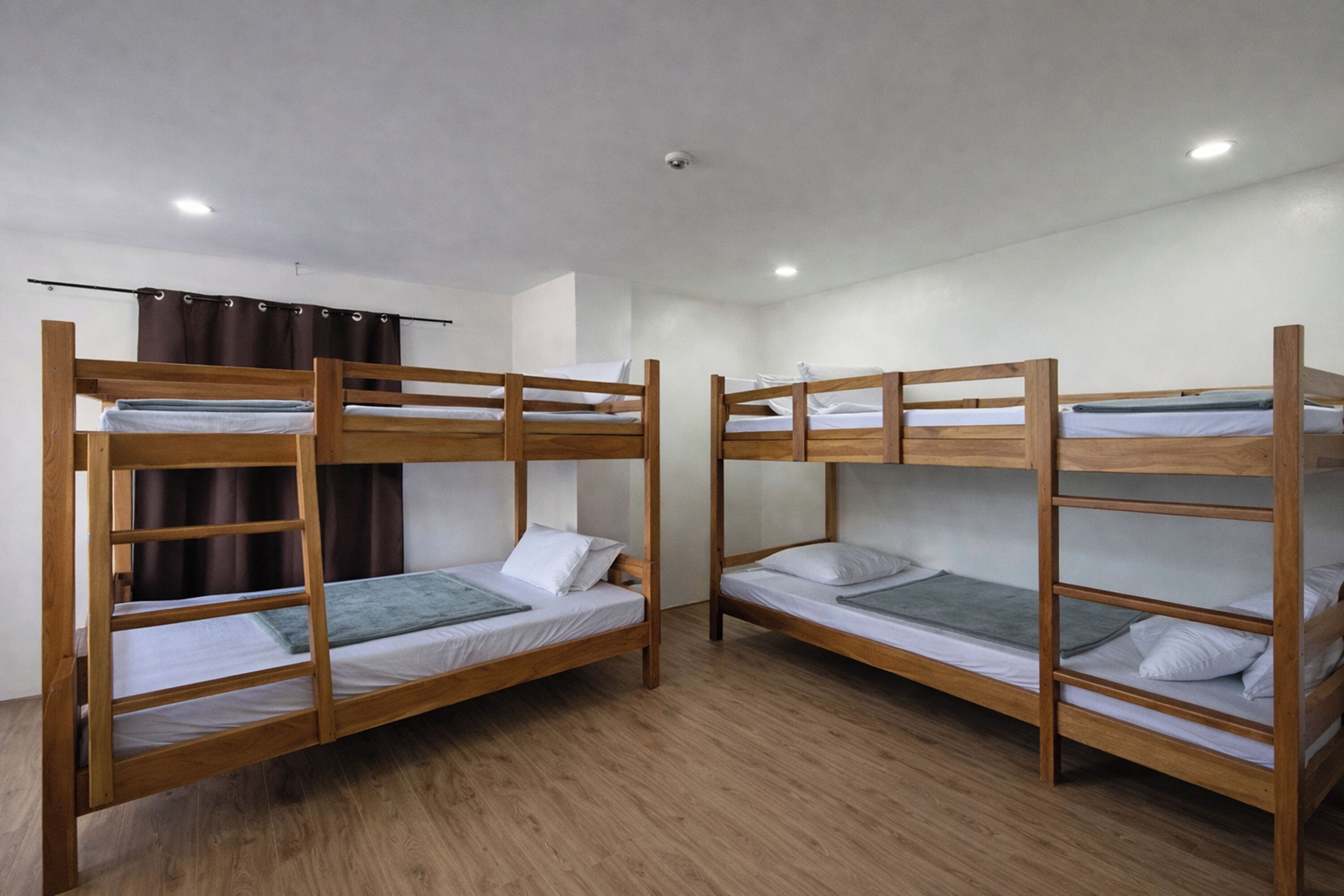 Una habitación con dos literas, suelo de madera, una lámpara en el techo y una cortina.