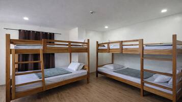 Una habitación con dos literas, suelo de madera, una lámpara en el techo y una cortina.
