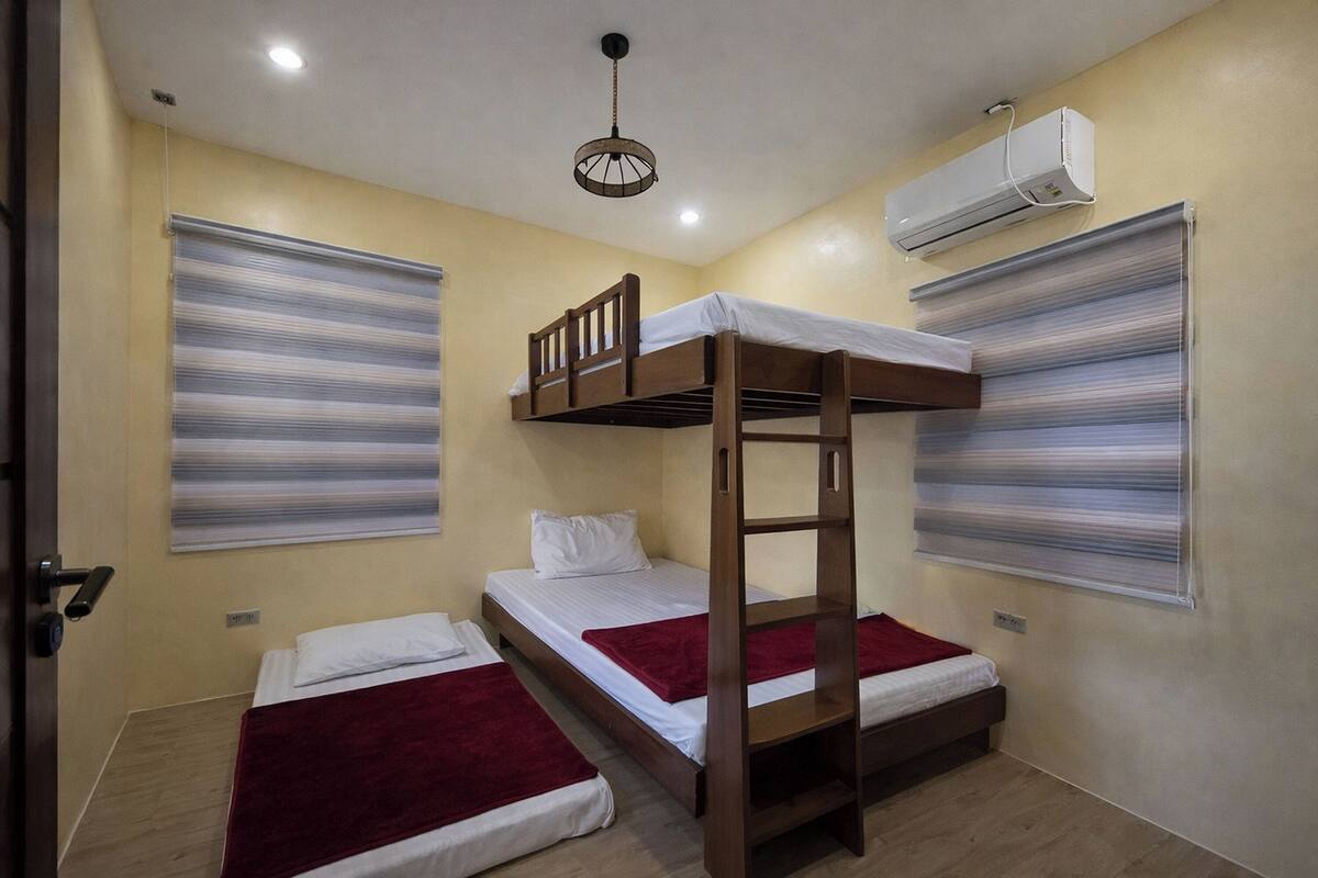 Una habitación con literas, una lámpara en el techo, un equipo de aire acondicionado y una ventana con persianas.