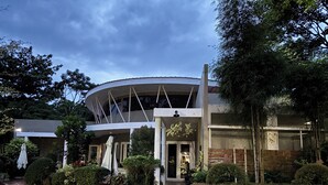 A modern building with a curved roof, a stone facade, and a well-maintained garden with hedges and trees. - Alejandro'S Suites & Venue (Valencia)